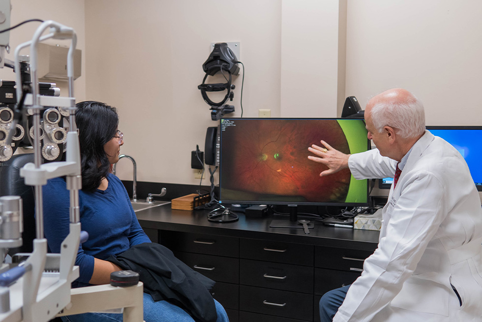 dr baker explains the results of an optical photo on a screen with a patient sitting and listening nearby