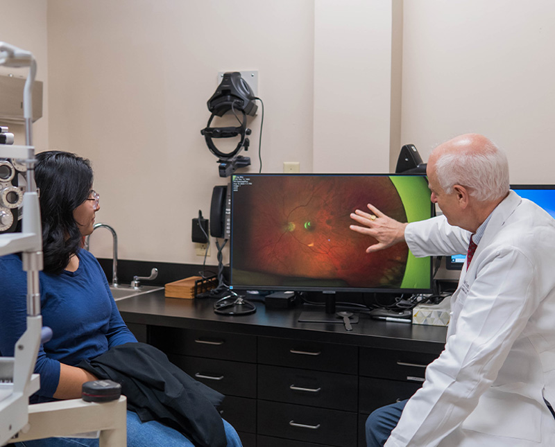 dr baker explains the results of an optical photo on a screen with a patient sitting and listening nearby