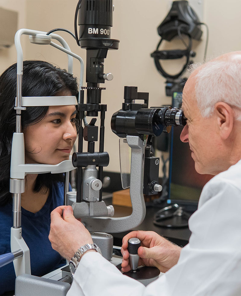 close up image of dr baker looking into an eye exam machine with a patient on the other side